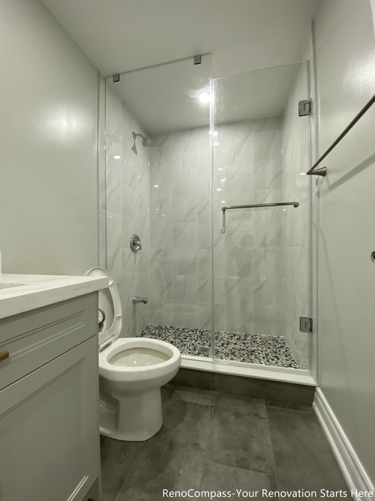 This Oakville basement bathroom renovation features a modern walk-in glass shower with marble-style wall tiles, pebble shower flooring, and sleek chrome fixtures for a clean and contemporary finish. The space is designed for both comfort and durability, combining water-resistant materials with efficient layout planning to maximize functionality in a compact basement setting. Completed by a trusted Toronto renovation company, this bathroom upgrade enhances daily living while adding long-term value and modern appeal to the home.