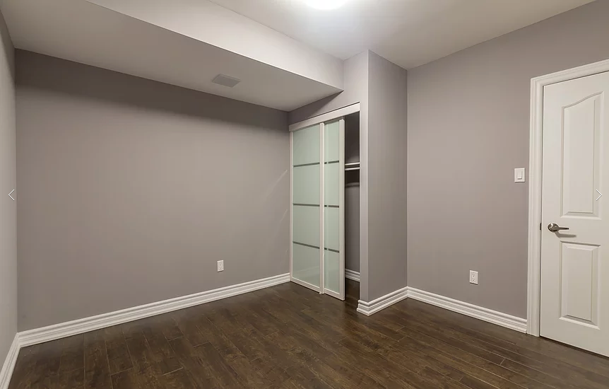 Newly finished basement bedroom completed in this Toronto basement renovation project. The space features modern grey wall finishes, upgraded hardwood flooring, a built-in closet with sliding glass doors, and clean baseboard detailing. Designed to add functional living space and increase home value, this basement room showcases professional craftsmanship by a trusted Toronto renovation company specializing in complete basement finishing and interior renovations.