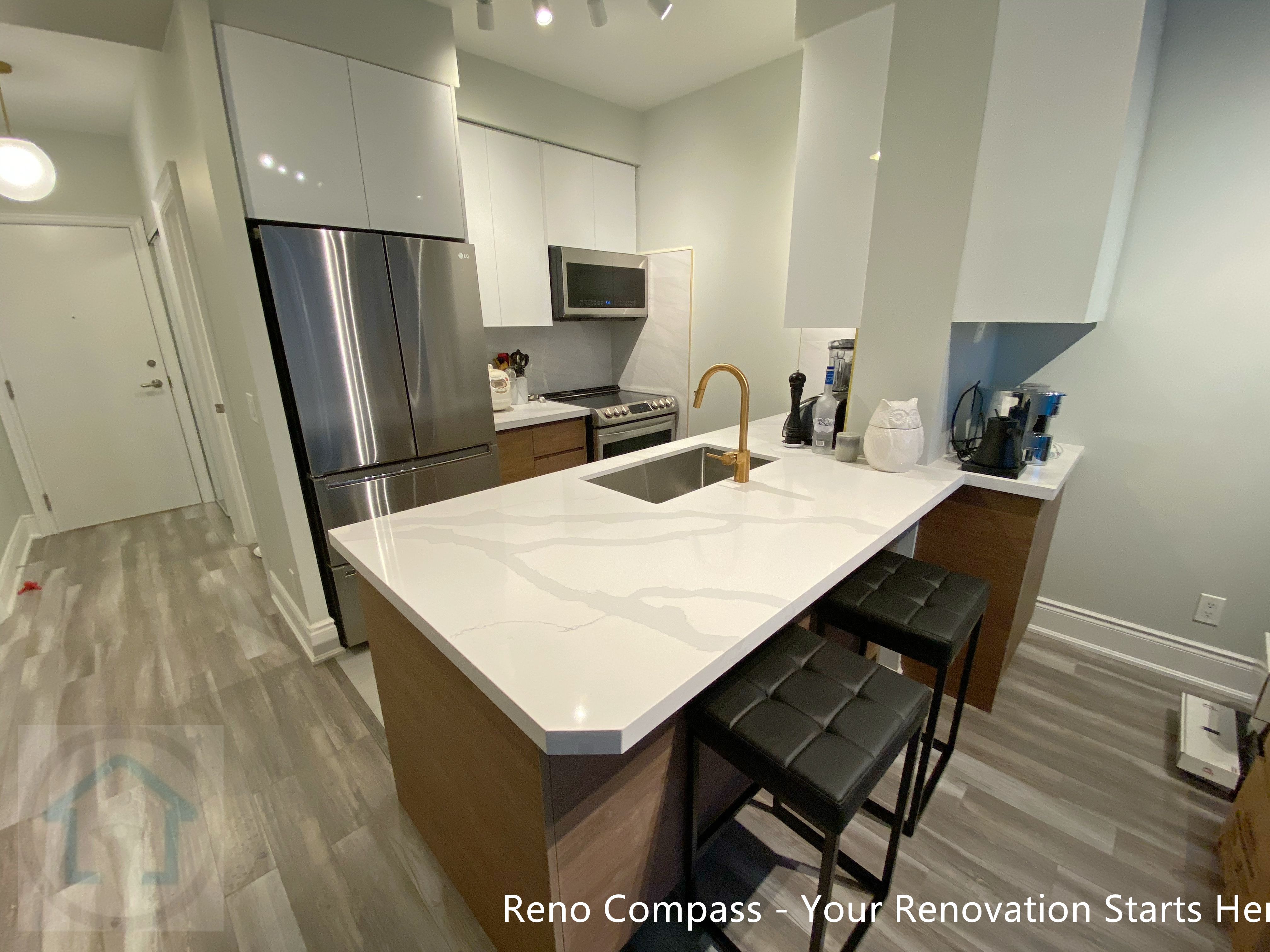 This North York condo kitchen renovation showcases a modern layout centered around a quartz waterfall island with integrated seating. White flat-panel cabinetry, stainless steel appliances, and a warm wood base create a balanced contrast between clean lines and natural tones. The redesigned kitchen improves storage efficiency, workflow, and everyday functionality, making it ideal for contemporary condo living and long-term value.