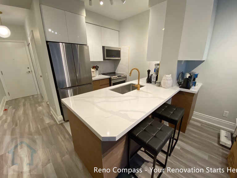 This North York condo kitchen renovation showcases a modern layout centered around a quartz waterfall island with integrated seating. White flat-panel cabinetry, stainless steel appliances, and a warm wood base create a balanced contrast between clean lines and natural tones. The redesigned kitchen improves storage efficiency, workflow, and everyday functionality, making it ideal for contemporary condo living and long-term value.