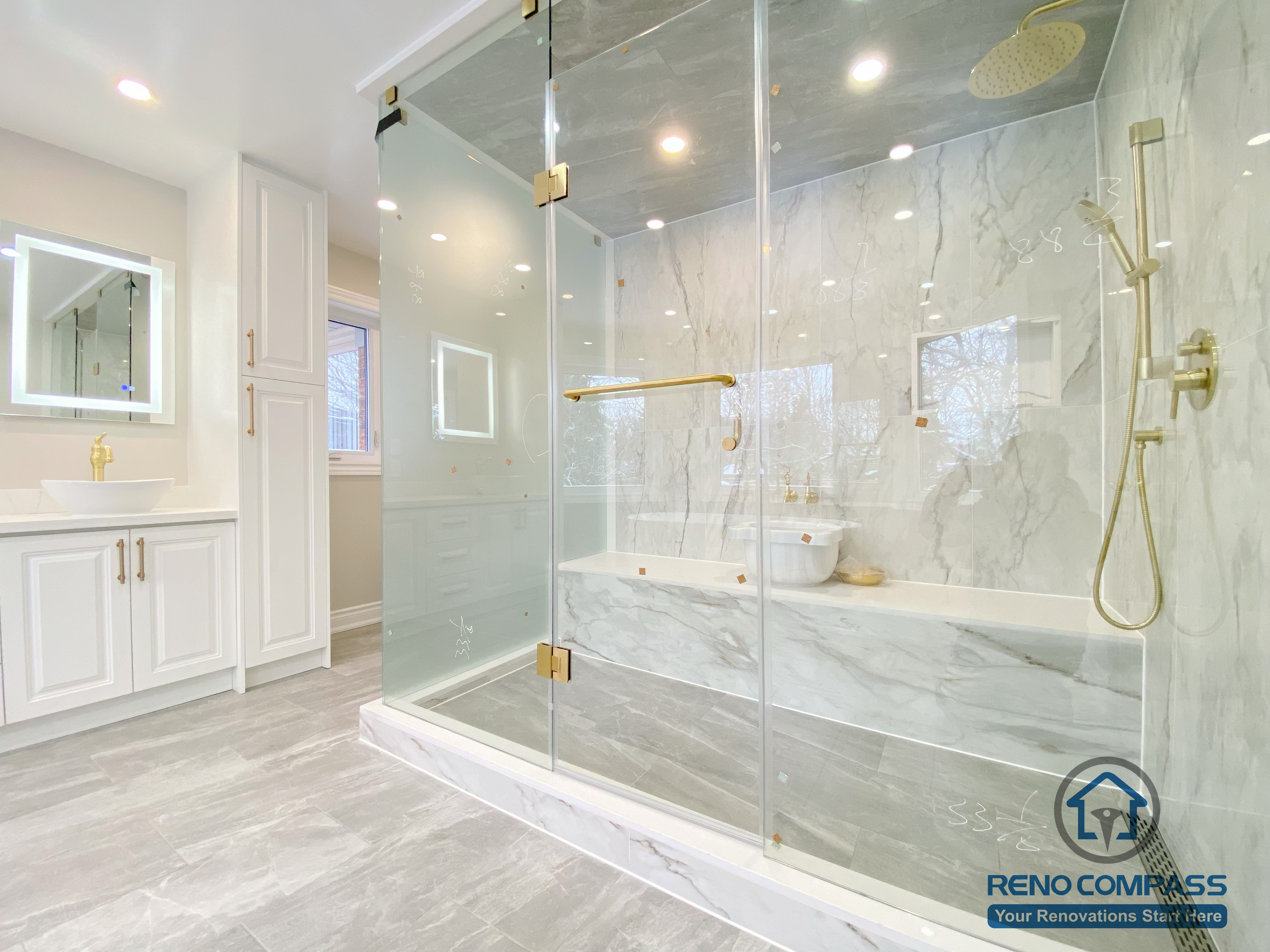 This Richmond Hill bathroom renovation showcases a bright and elegant design featuring a frameless glass shower enclosure, built-in bathtub, marble-style wall tiles, and gold-finish fixtures. The custom white vanity with integrated lighting mirror and large-format floor tiles enhance both functionality and visual openness. This project reflects high-quality craftsmanship and thoughtful layout planning for a modern bathroom renovation in Richmond Hill.