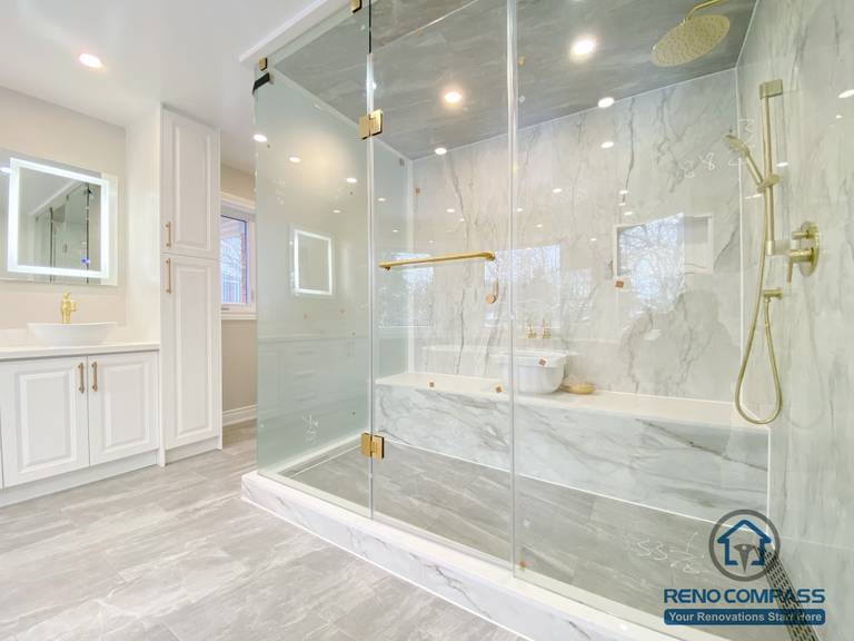 This Richmond Hill bathroom renovation showcases a bright and elegant design featuring a frameless glass shower enclosure, built-in bathtub, marble-style wall tiles, and gold-finish fixtures. The custom white vanity with integrated lighting mirror and large-format floor tiles enhance both functionality and visual openness. This project reflects high-quality craftsmanship and thoughtful layout planning for a modern bathroom renovation in Richmond Hill.