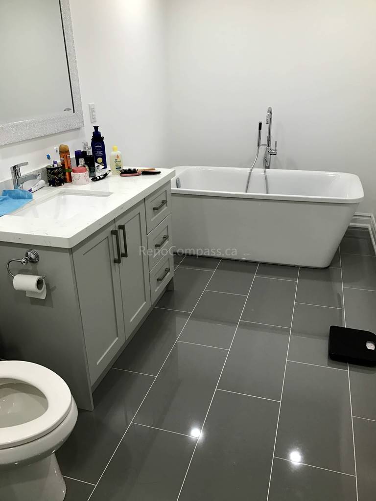This Toronto bathroom renovation by Reno Compass features a sleek freestanding bathtub paired with a custom vanity and quartz countertop. Large-format grey floor tiles create a clean and contemporary look, while modern fixtures and a spacious layout enhance comfort and functionality. Designed for both relaxation and everyday convenience, this upgraded bathroom combines elegant finishes with durable craftsmanship to increase long-term home value.
