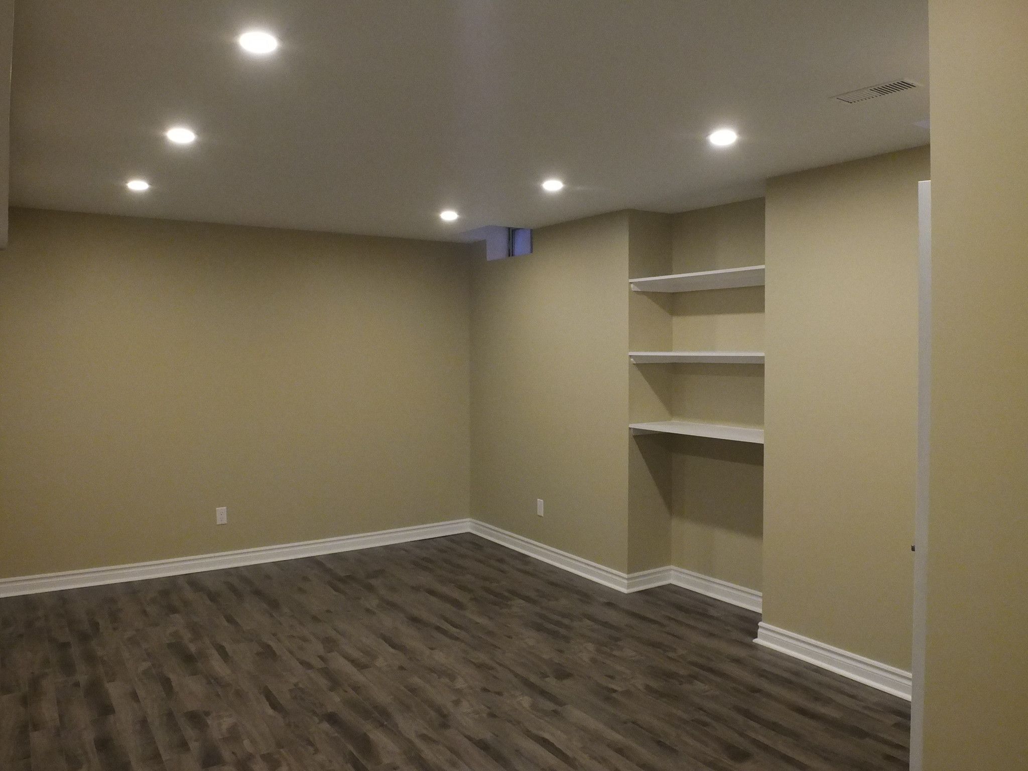 This Vaughan basement renovation showcases a clean and functional finished space designed by a professional Toronto Renovation Company. The layout features modern recessed pot lighting, durable wood-look flooring, and custom built-in shelving that provides both storage and decorative display options. Neutral wall tones and thoughtful lighting placement create a warm and inviting environment, ideal for a family lounge, entertainment room, or home office. The finished basement enhances everyday living while adding long-term property value for homeowners across the GTA.