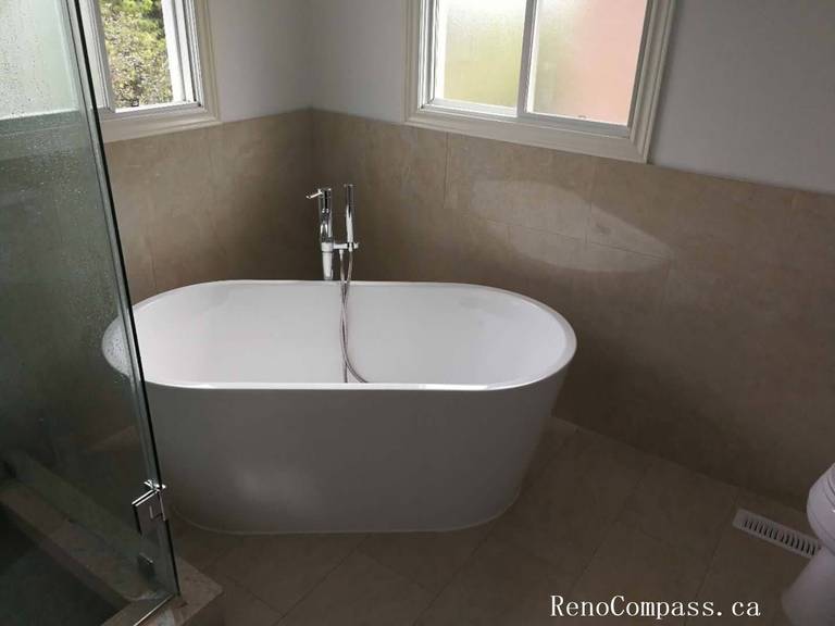 This image showcases a modern basement bathroom renovation in Richmond Hill featuring a sleek freestanding bathtub, frameless glass shower enclosure, and light porcelain tile finishes. Professionally completed by Reno Compass Inc., the design creates a bright, spa‑like space while enhancing overall basement functionality.