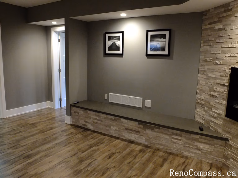 Modern finished basement in Waterloo featuring a stunning stone feature wall, built‑in electric fireplace, recessed lighting, and a custom bench with matching stone accents. A stylish focal point in the renovated lower level.