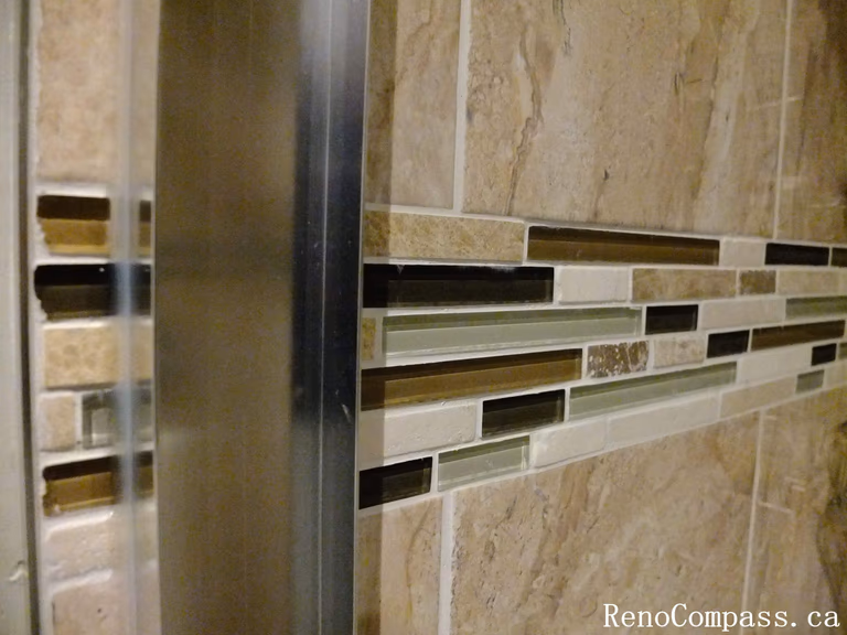 Accent tile detail from a North York bathroom renovation, featuring a horizontal glass mosaic band integrated with wall tiles for added depth, texture, and a refined shower design.