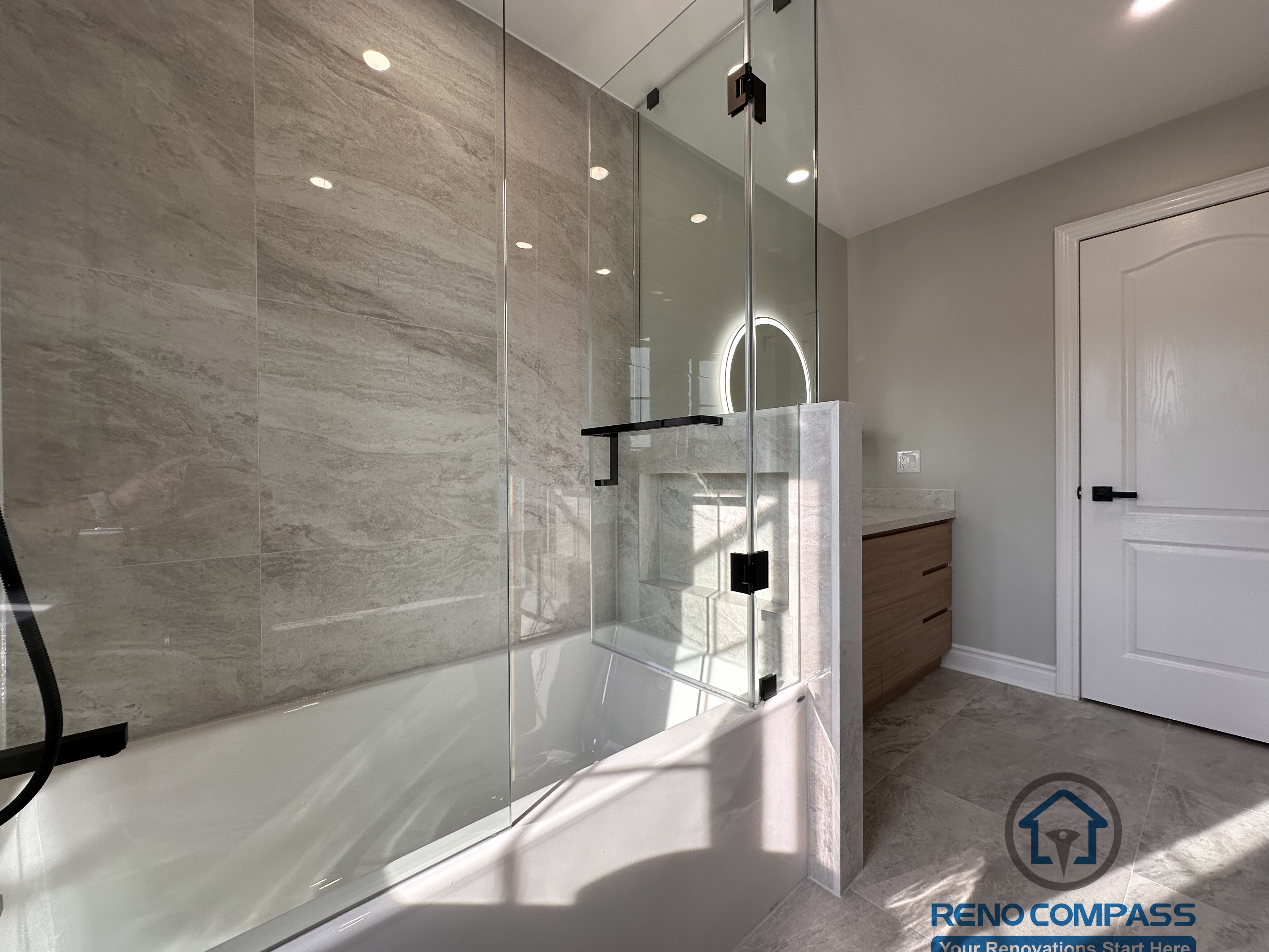 This Markham bathroom renovation highlights a glass-enclosed tub and shower combination with full-height stone-look wall tiles and matte black hardware. The design maintains openness while ensuring practical water control and durability. Completed by a professional Toronto renovation company, Reno Compass Inc., the bathroom reflects clean detailing, balanced proportions, and long-term functionality.