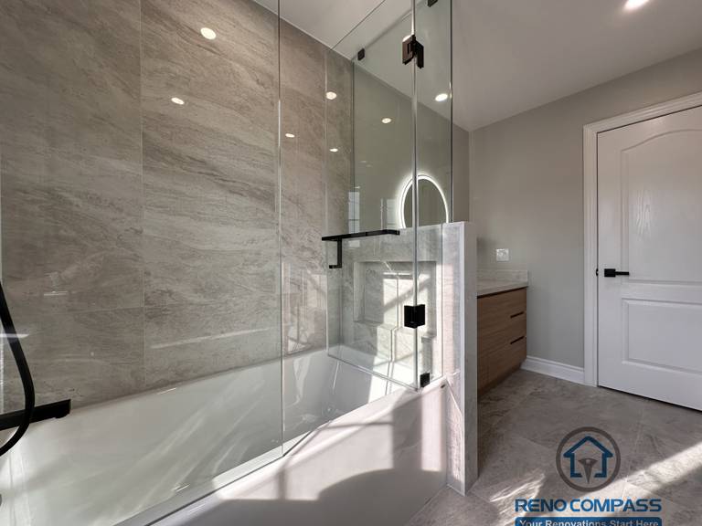 This Markham bathroom renovation highlights a glass-enclosed tub and shower combination with full-height stone-look wall tiles and matte black hardware. The design maintains openness while ensuring practical water control and durability. Completed by a professional Toronto renovation company, Reno Compass Inc., the bathroom reflects clean detailing, balanced proportions, and long-term functionality.