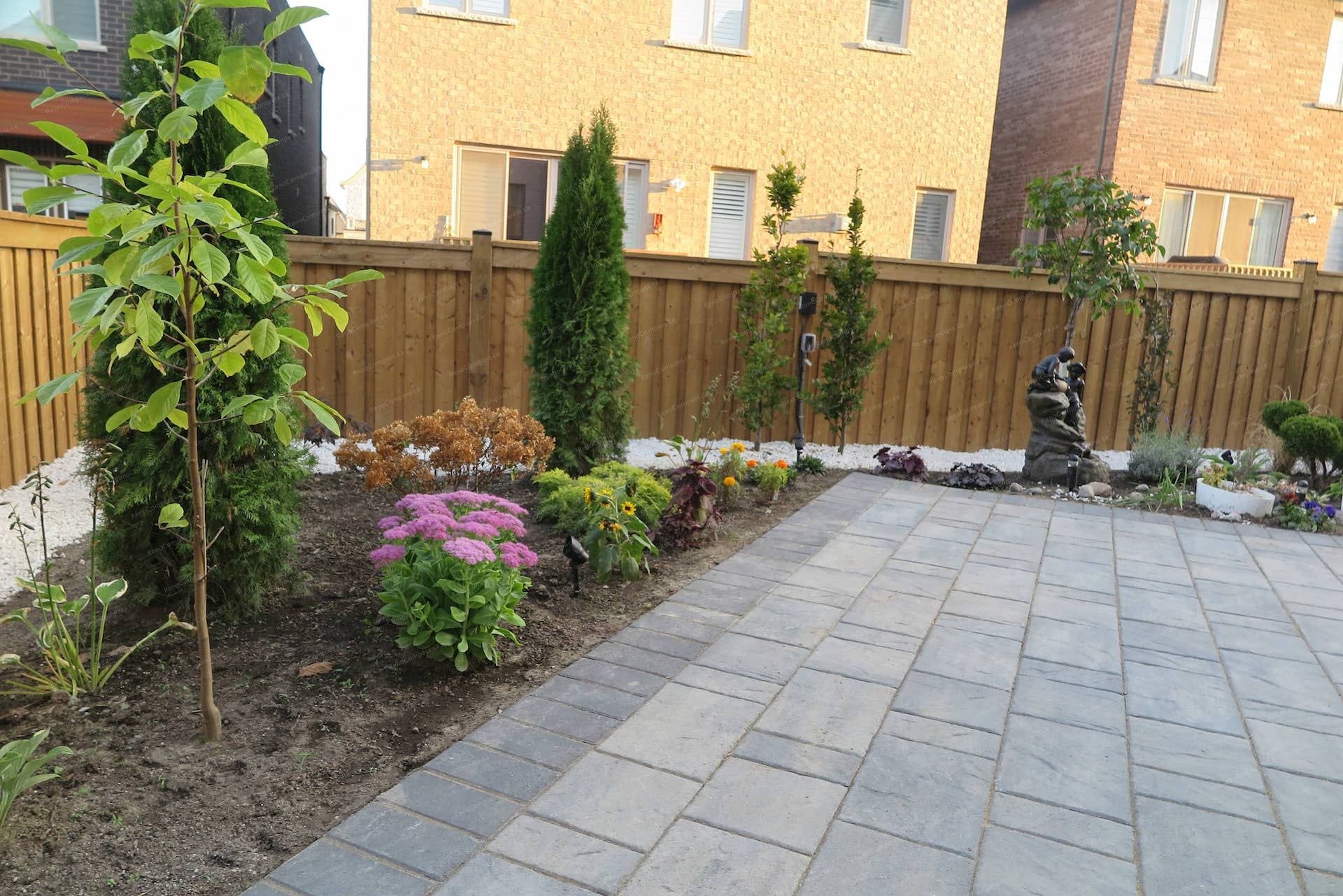 This Vaughan landscaping renovation features a modern interlock patio combined with a carefully arranged garden bed, decorative river rocks, and ornamental plants. The design integrates natural textures, structured greenery, and landscape accents to create a relaxing and visually balanced backyard environment. Professionally completed by Reno Compass Inc.
