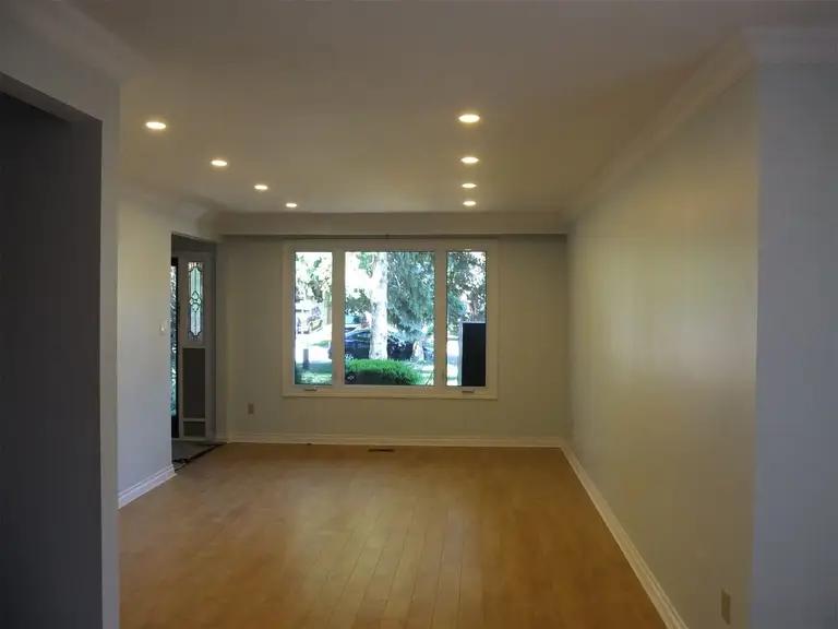 This Oshawa interior renovation highlights a fully refreshed living room with upgraded recessed pot lights, smooth ceiling finish, and newly refinished hardwood flooring. The large front-facing window enhances natural daylight, creating a bright and welcoming atmosphere. Neutral wall tones combined with detailed crown molding provide a clean and modern aesthetic. The optimized lighting layout improves both functionality and visual depth of the space. Completed by a professional Toronto Renovation Company, this project demonstrates quality craftsmanship and thoughtful interior enhancement.