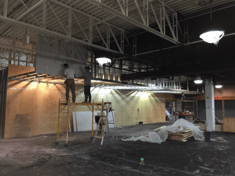 This image captures the construction phase of an outdoor retail store renovation, featuring structural ceiling framing, custom wood wall installation, and lighting preparation. The team is installing overhead framing and wood panel backdrops to support future retail displays and shelving systems. Reno Compass Inc. ensures precise craftsmanship and proper structural alignment during every stage of the commercial renovation process, building a durable and well-designed retail environment from the ground up.