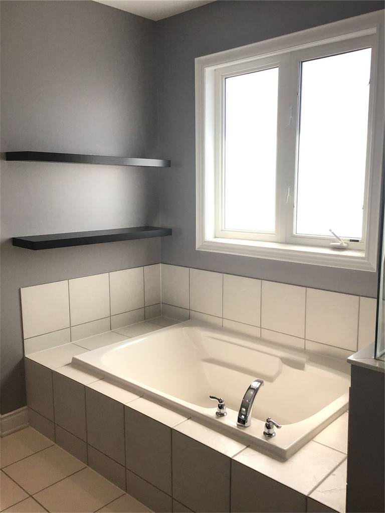 This Markham full home renovation features a clean and modern bathroom with a built-in soaking tub, tiled surround, and natural light from a large window. The minimalist design, neutral color palette, and functional shelving create a relaxing and spa-like atmosphere. Completed by a trusted Toronto Renovation Company, this space combines comfort with practical design.