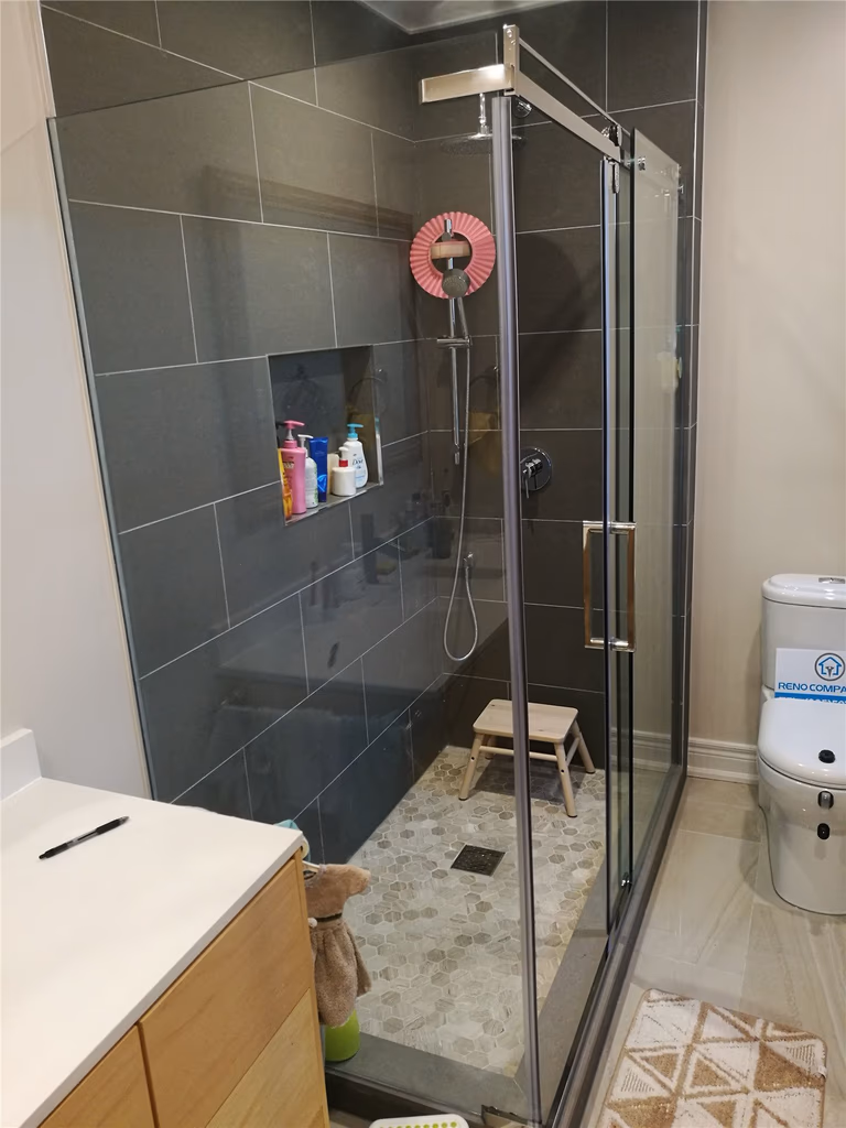 This Richmond Hill bathroom renovation features a modern glass walk-in shower with dark large-format wall tiles, built-in storage niche, and a sleek chrome shower system. The spacious layout, slip-resistant shower flooring, and contemporary vanity create a functional and stylish bathroom upgrade. Completed by a professional Toronto renovation company, this project highlights quality craftsmanship, efficient space planning, and durable materials designed for everyday comfort and long-term performance.