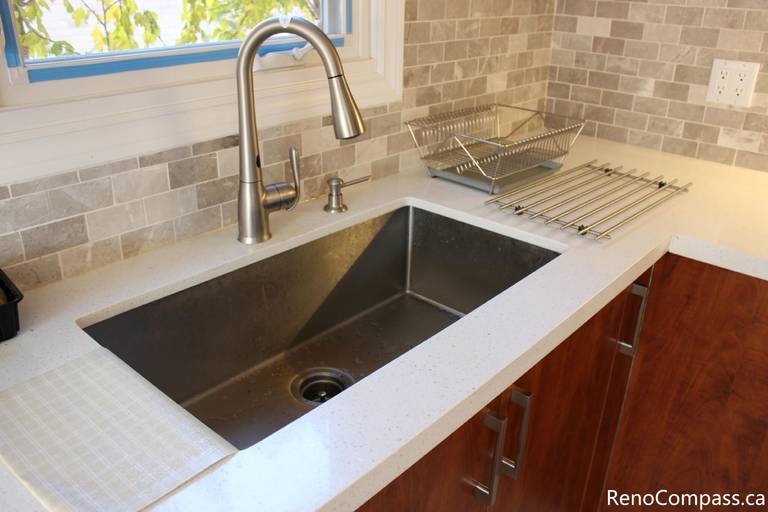 This close-up kitchen detail showcases a modern stainless steel undermount sink, sleek pull-down faucet, and durable quartz countertop installed as part of a full house renovation in Mississauga. The neutral mosaic backsplash and upgraded fixtures enhance both functionality and visual appeal, creating a clean and contemporary workspace. Completed by a professional Toronto renovation company, this renovation focuses on quality materials, practical design, and long-term everyday comfort for homeowners.