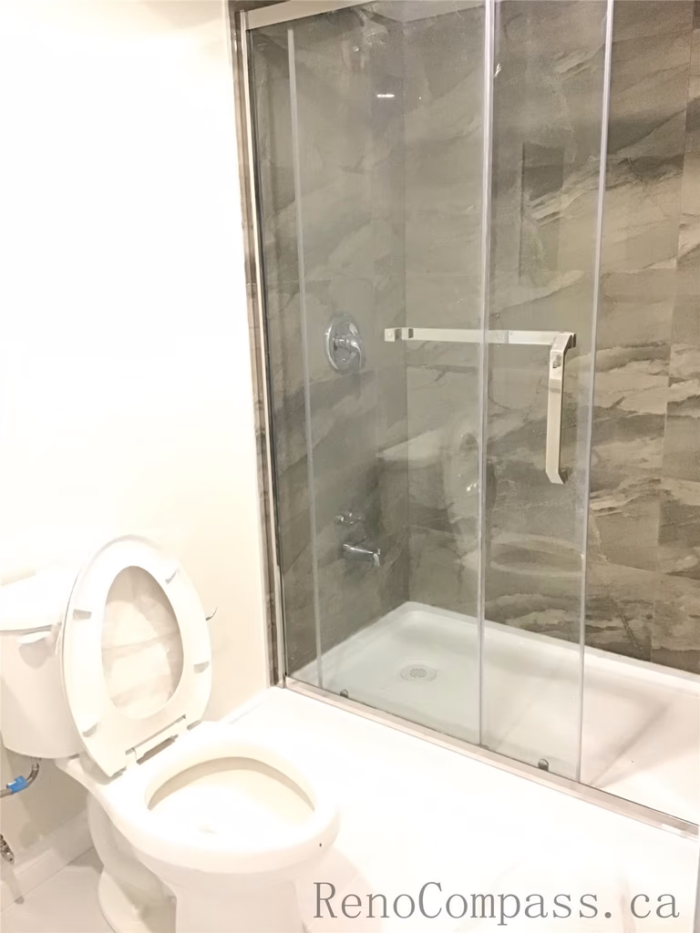 Modern basement bathroom renovation in Whitby featuring a sliding glass shower enclosure, contemporary gray wall tiles, and clean white fixtures. The space is thoughtfully designed to maximize functionality while maintaining a sleek and low-maintenance finish. Completed by a trusted Toronto renovation company, this Whitby basement project showcases quality tile work and precise bathroom installation craftsmanship.