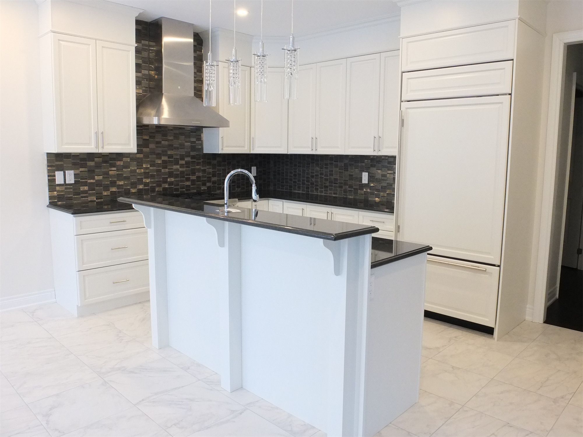 This Kleinburg interior renovation features a bright and elegant modern kitchen with custom white cabinetry, marble-style flooring, and a functional island with built-in sink. The design combines clean lines, stainless steel appliances, and a dark mosaic backsplash to create a refined contrast while maintaining a spacious and contemporary feel. The kitchen island also provides additional workspace and seating, making the space both stylish and highly practical for everyday living.