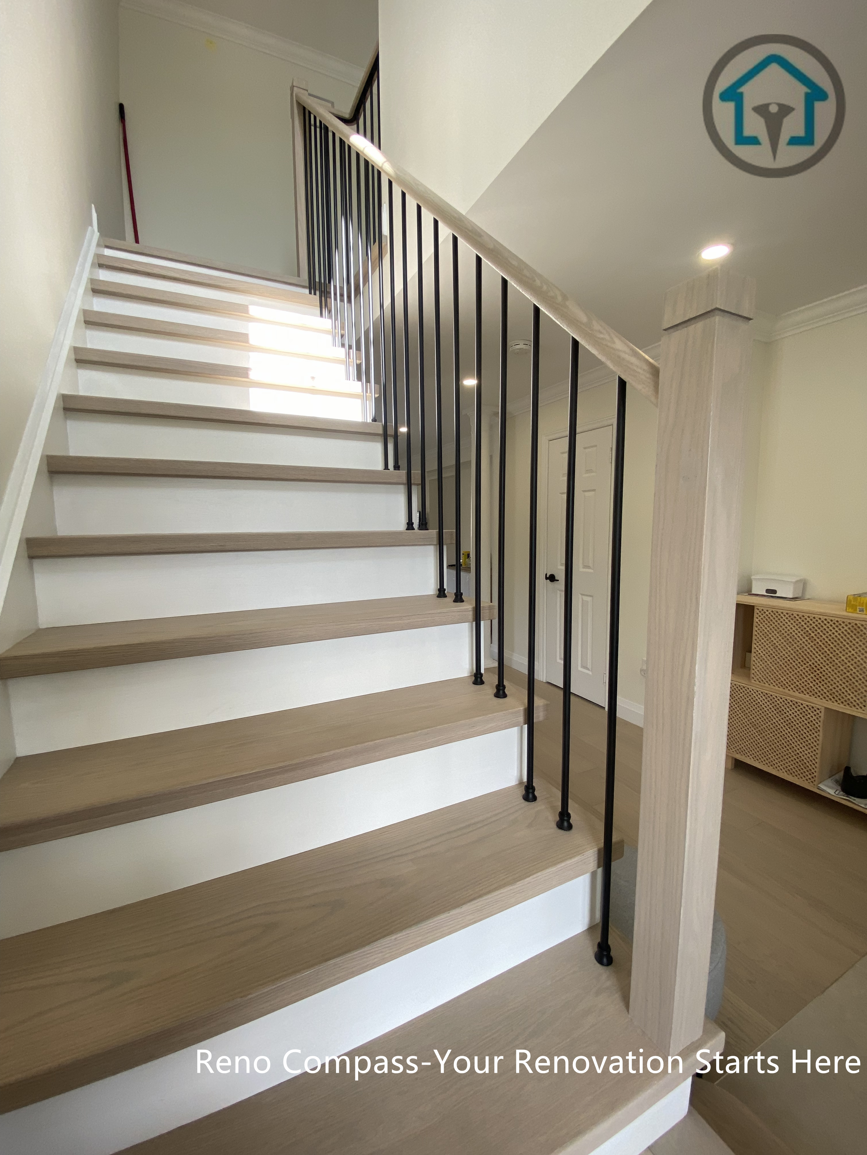 Modern flooring and staircase renovation in Markham featuring light oak hardwood floors, white riser stairs, and black iron balusters. The open staircase design enhances natural light flow and creates a clean, contemporary interior transition between floors. Completed by a professional Toronto renovation company with a focus on durability, safety, and timeless aesthetics.