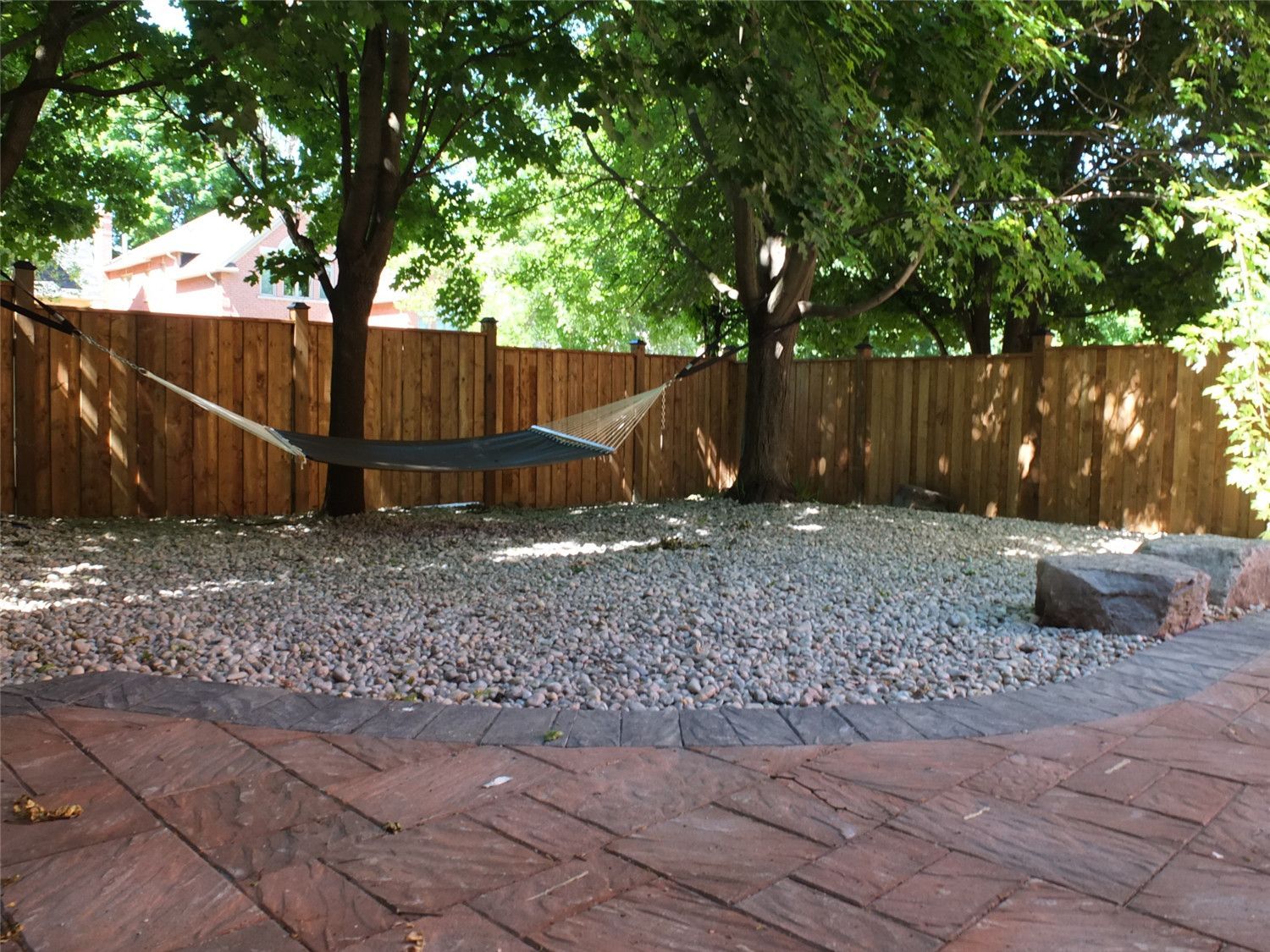 This Aurora landscaping renovation highlights a curved interlocking patio seamlessly integrated with a decorative gravel relaxation area. The contrasting stone border defines the transition between the paver surface and the natural stone feature zone, creating visual depth and balance.

Reno Compass Inc. carefully designed the layout to preserve mature trees while enhancing usability. The addition of river stone, large accent rocks, and a hammock-ready space transforms the backyard into a tranquil retreat that blends structure with nature.