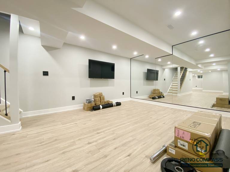 This Aurora basement renovation showcases a spacious entertainment and multi-purpose area featuring a full mirror wall, wall-mounted TV, recessed ceiling lighting, and wood-look flooring. The mirrored surface enhances visual depth and brightness, making the space suitable for home entertainment, fitness, or flexible recreational use. Completed by a Toronto renovation company, this basement renovation highlights adaptable space planning and modern interior finishes.