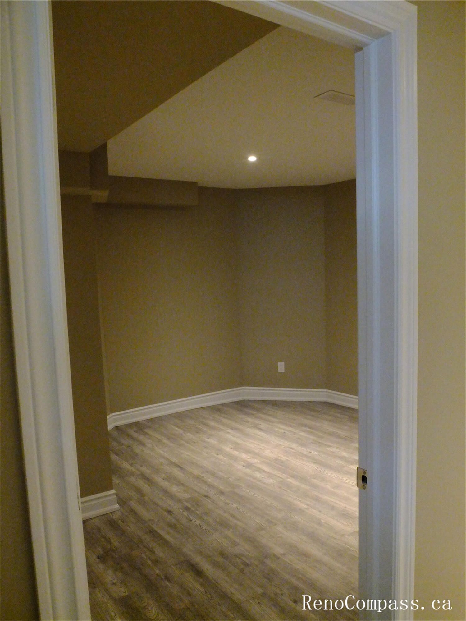 View of a finished basement room in this Ajax basement renovation, featuring durable vinyl plank flooring, neutral wall tones, and recessed pot lights for bright, even lighting. The clean layout and modern finishes make this space ideal for a home office, guest room, or recreation area. Completed by a professional Toronto Renovation Company, the renovation focuses on comfort, functionality, and long-lasting materials suitable for basement living spaces.