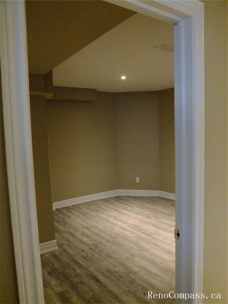 View of a finished basement room in this Ajax basement renovation, featuring durable vinyl plank flooring, neutral wall tones, and recessed pot lights for bright, even lighting. The clean layout and modern finishes make this space ideal for a home office, guest room, or recreation area. Completed by a professional Toronto Renovation Company, the renovation focuses on comfort, functionality, and long-lasting materials suitable for basement living spaces.