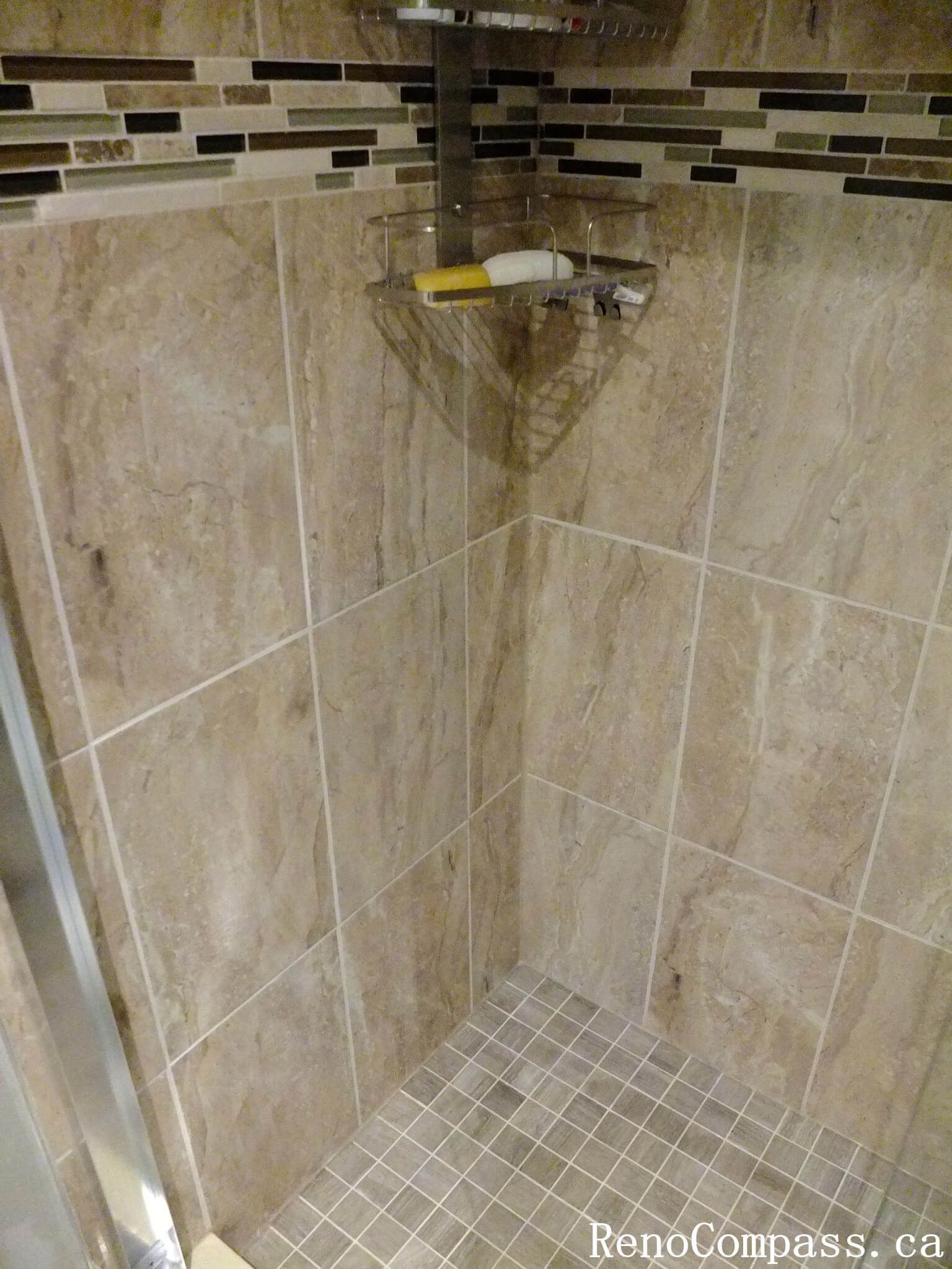 Shower area detail from a North York bathroom renovation, featuring full-height wall tiles, mosaic accent band, and slip-resistant floor tiles with clean grout lines and precise craftsmanship.