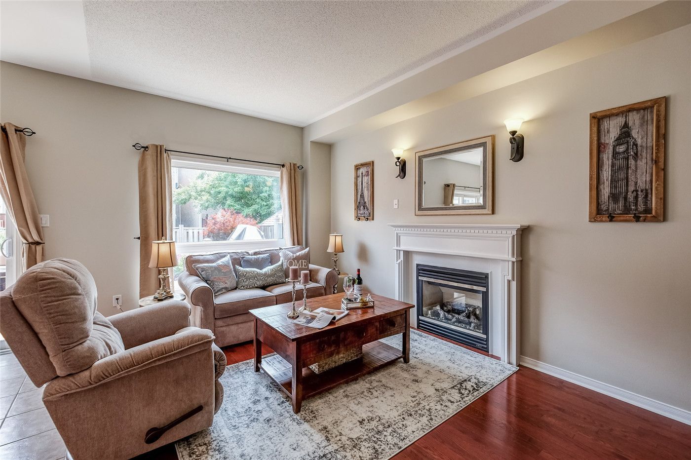 This Toronto interior design pre-sale staging showcases a warm and inviting living room featuring a modern fireplace, hardwood flooring, neutral-tone furniture, and elegant wall décor. Large windows bring in natural light while soft furnishings and a coordinated layout create a reminder of comfort and space.