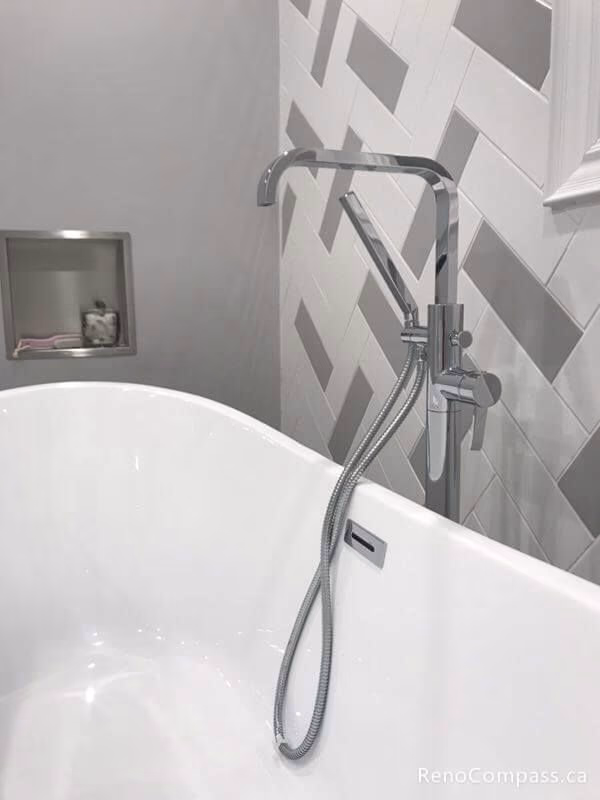 A close-up view of a luxury bathroom renovation in Markham. Showcasing a sleek chrome standing faucet, a white soaking tub, and custom grey and white herringbone wall tiling.