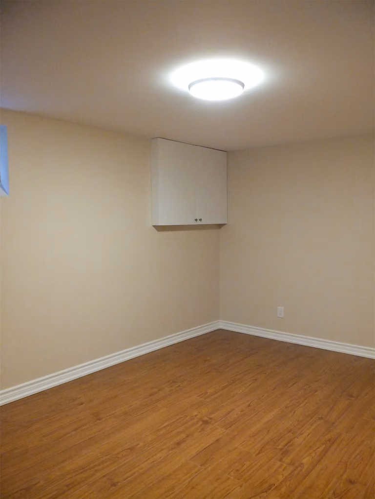 This Markham basement renovation project features newly finished walls, fresh interior painting, and durable laminate flooring installation. The clean wall finish, neutral paint tones, and wood-style flooring create a bright, comfortable living space suitable for a family recreation room or additional living area. Careful detailing around the baseboards and wall edges ensures a smooth and polished appearance throughout the basement interior.