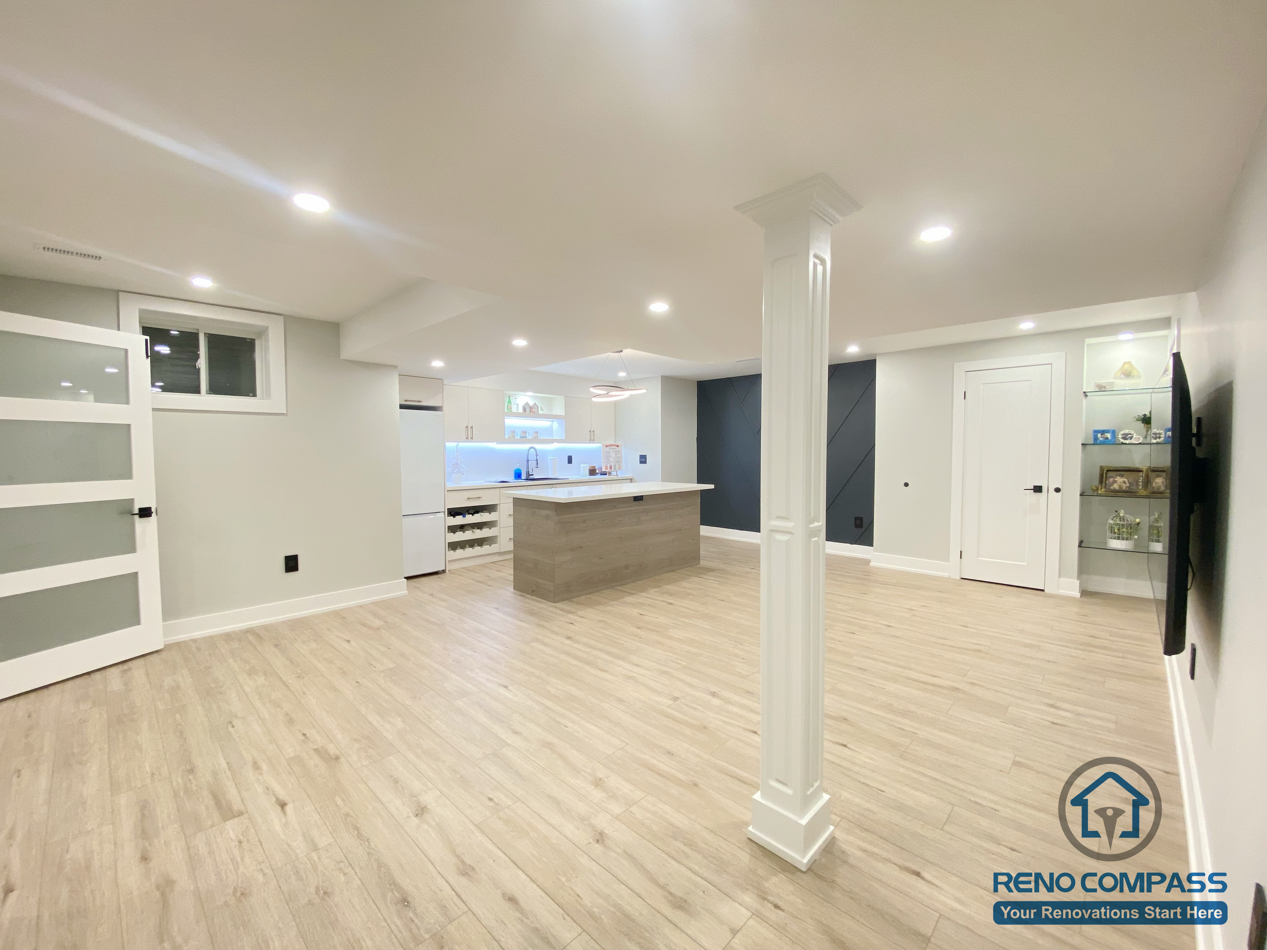 This Aurora basement renovation features a wide open-concept layout that integrates the kitchen, living, and multi-purpose areas while maintaining clear structural organization. The design includes a central support column, wood-look flooring, recessed ceiling lighting, and a bright, neutral color palette that enhances spatial openness. Completed by a Toronto renovation company, this basement renovation demonstrates efficient structural planning and modern design suited for flexible lower-level living.