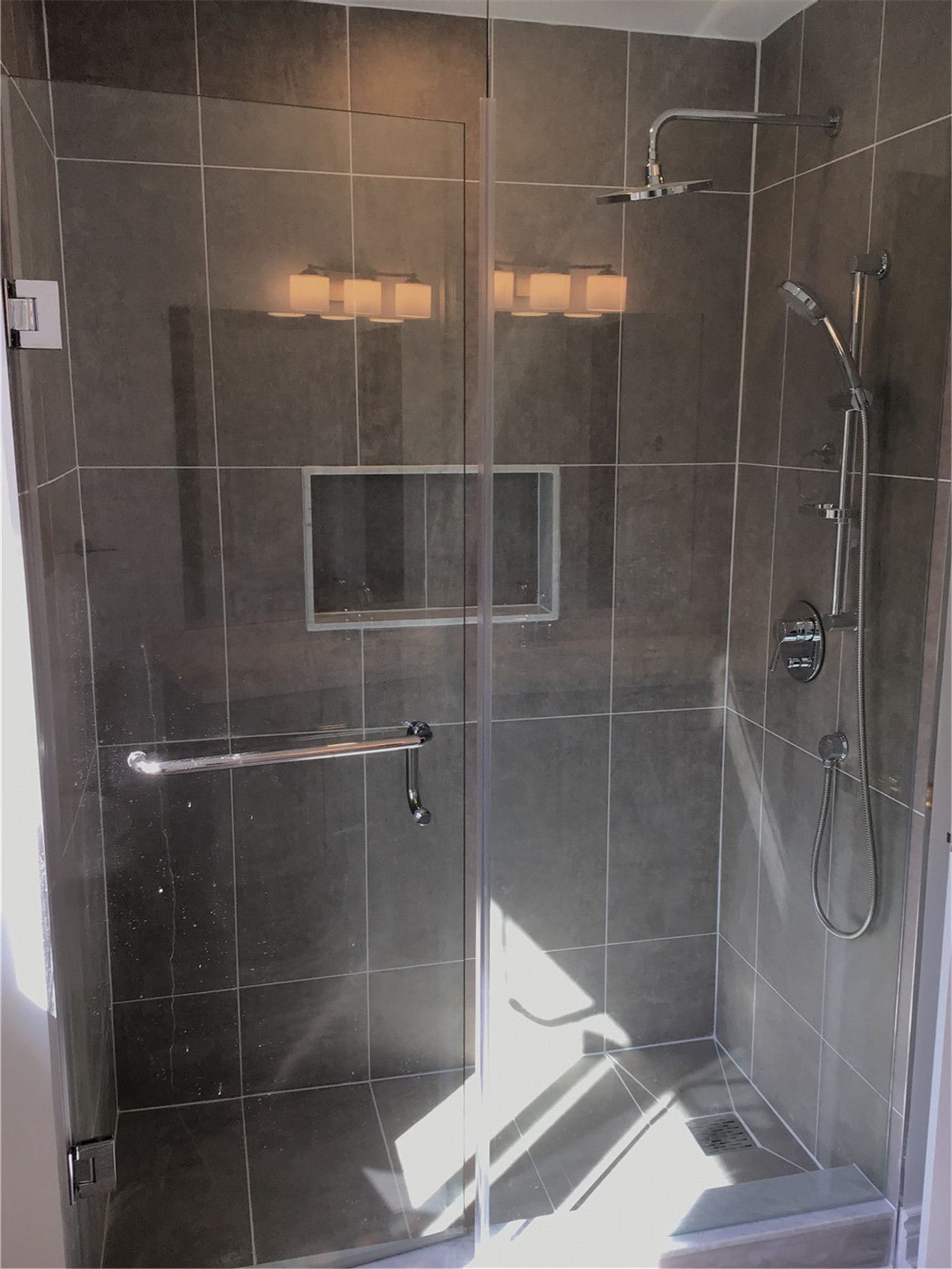 This Woodbridge bathroom renovation features a sleek walk-in shower with a frameless glass enclosure, large-format wall tiles, and a built-in niche for storage. The modern shower system with dual fixtures enhances both functionality and comfort, creating a clean and contemporary bathing space.