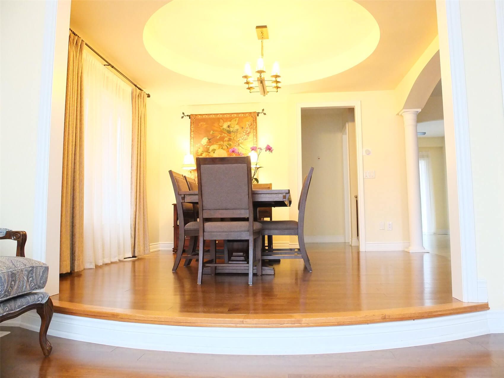 This Aurora flooring renovation highlights a beautifully upgraded dining room featuring rich hardwood flooring and elegant interior details. The polished wood floor complements the elevated dining area, curved step design, and warm ceiling lighting, creating a sophisticated and inviting atmosphere. Completed by a professional Toronto renovation company, the flooring installation enhances both the visual appeal and durability of this refined dining space.