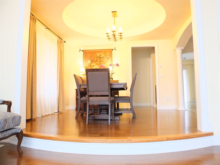 This Aurora flooring renovation highlights a beautifully upgraded dining room featuring rich hardwood flooring and elegant interior details. The polished wood floor complements the elevated dining area, curved step design, and warm ceiling lighting, creating a sophisticated and inviting atmosphere. Completed by a professional Toronto renovation company, the flooring installation enhances both the visual appeal and durability of this refined dining space.