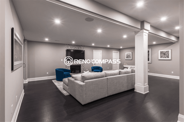 Spacious open-concept basement renovation in Toronto featuring modern recessed lighting, dark hardwood flooring, structural support columns, and a comfortable entertainment lounge area. This elegant basement living space was professionally designed and completed by a trusted Toronto renovation company, Reno Compass Inc.