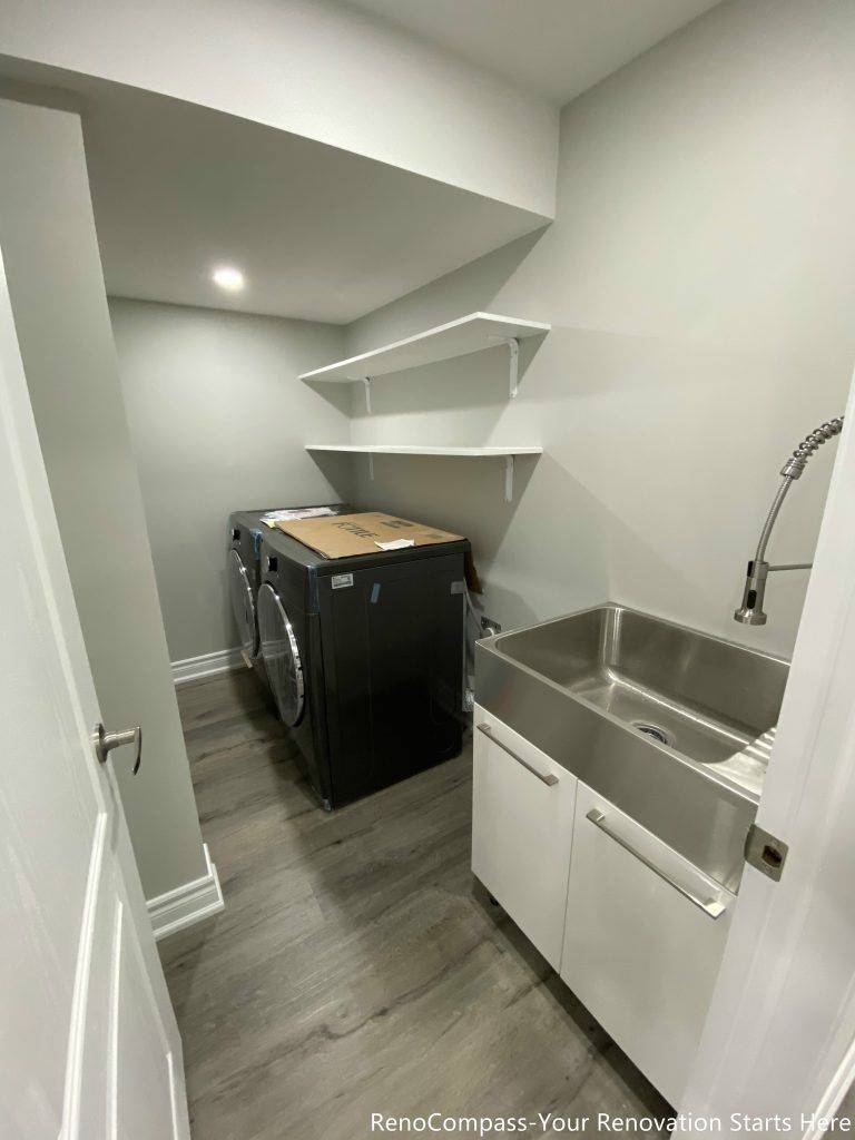 This Oakville basement renovation features a modern laundry room with upgraded flooring, a stainless steel utility sink, and custom wall shelving for efficient storage. The clean layout maximizes functionality while maintaining a bright and organized workspace for daily use. Designed and completed by a trusted Toronto renovation company, this basement laundry upgrade improves convenience, durability, and overall home value while creating a practical and well-designed utility space.