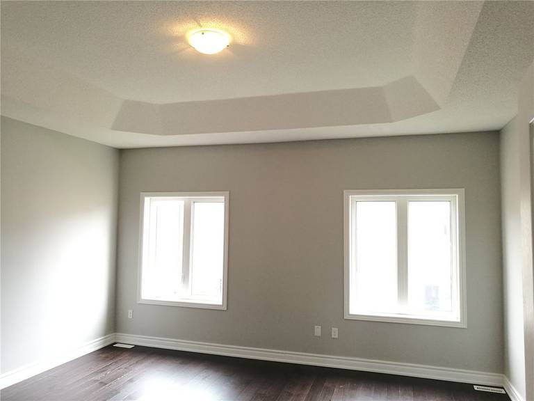 This image shows a bedroom after a Markham interior renovation, featuring a tray ceiling design, soft neutral wall colors, large windows for natural light, and dark hardwood flooring that creates a calm and balanced living environment.