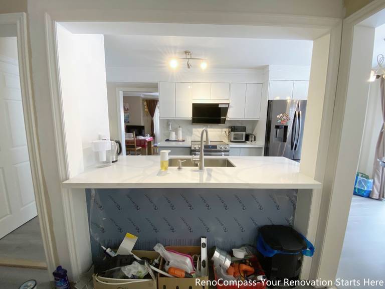 This image highlights an open-concept kitchen renovation in Mississauga featuring a pass-through counter that connects the kitchen to the adjacent living space. The design includes a quartz countertop with an integrated sink and modern faucet, creating a functional prep and serving area. White cabinetry, stainless steel appliances, and clean sightlines improve brightness and flow throughout the kitchen. This layout enhances interaction between spaces while maintaining practical work zones, making it a popular choice for contemporary Mississauga kitchen renovations.