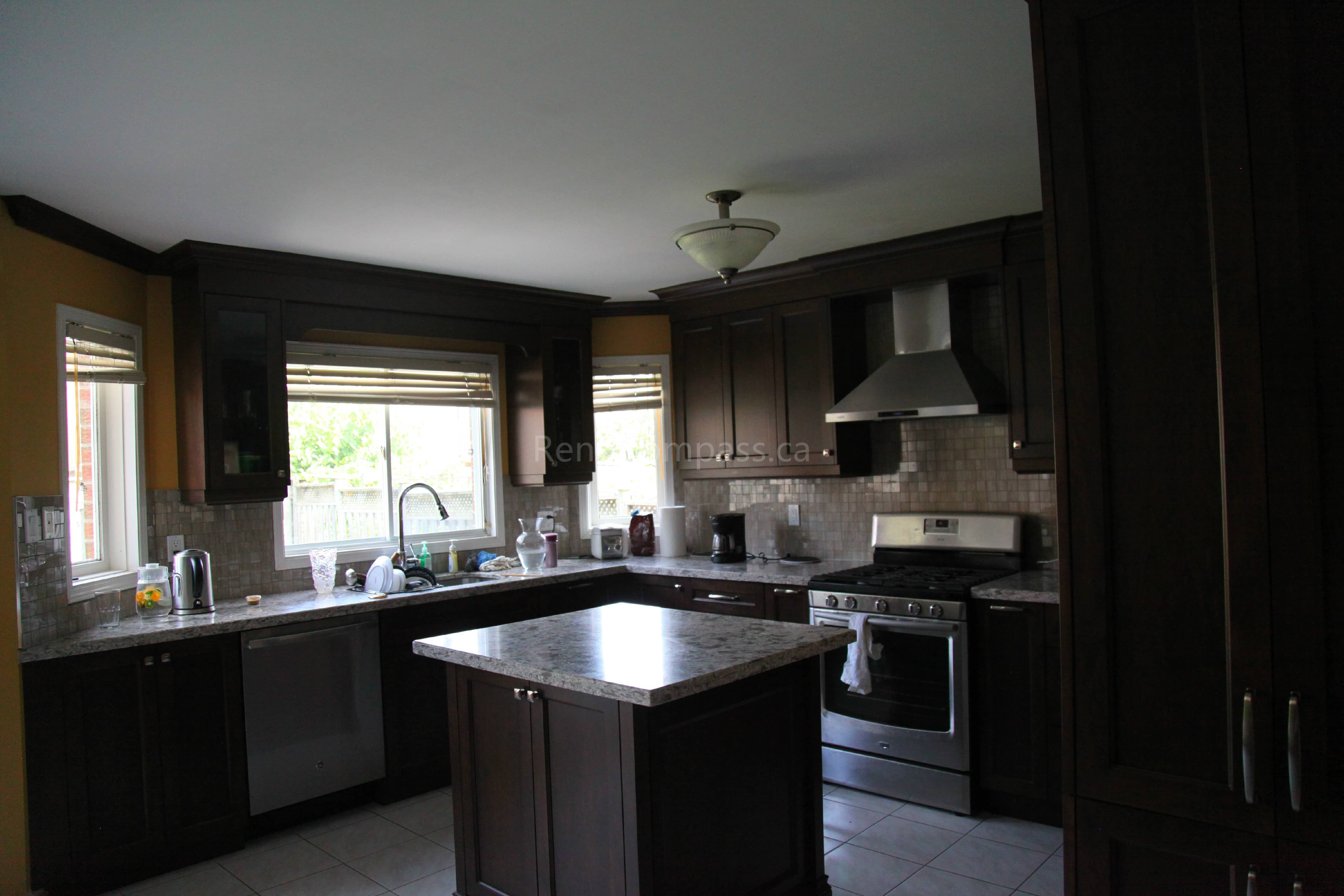 This Markham kitchen renovation features rich dark wood cabinetry, a custom quartz island, and modern stainless steel appliances, creating a warm and functional cooking space. Designed and completed by a professional Toronto renovation company, the layout enhances storage, workflow, and overall visual appeal while maintaining a timeless and elegant kitchen design.