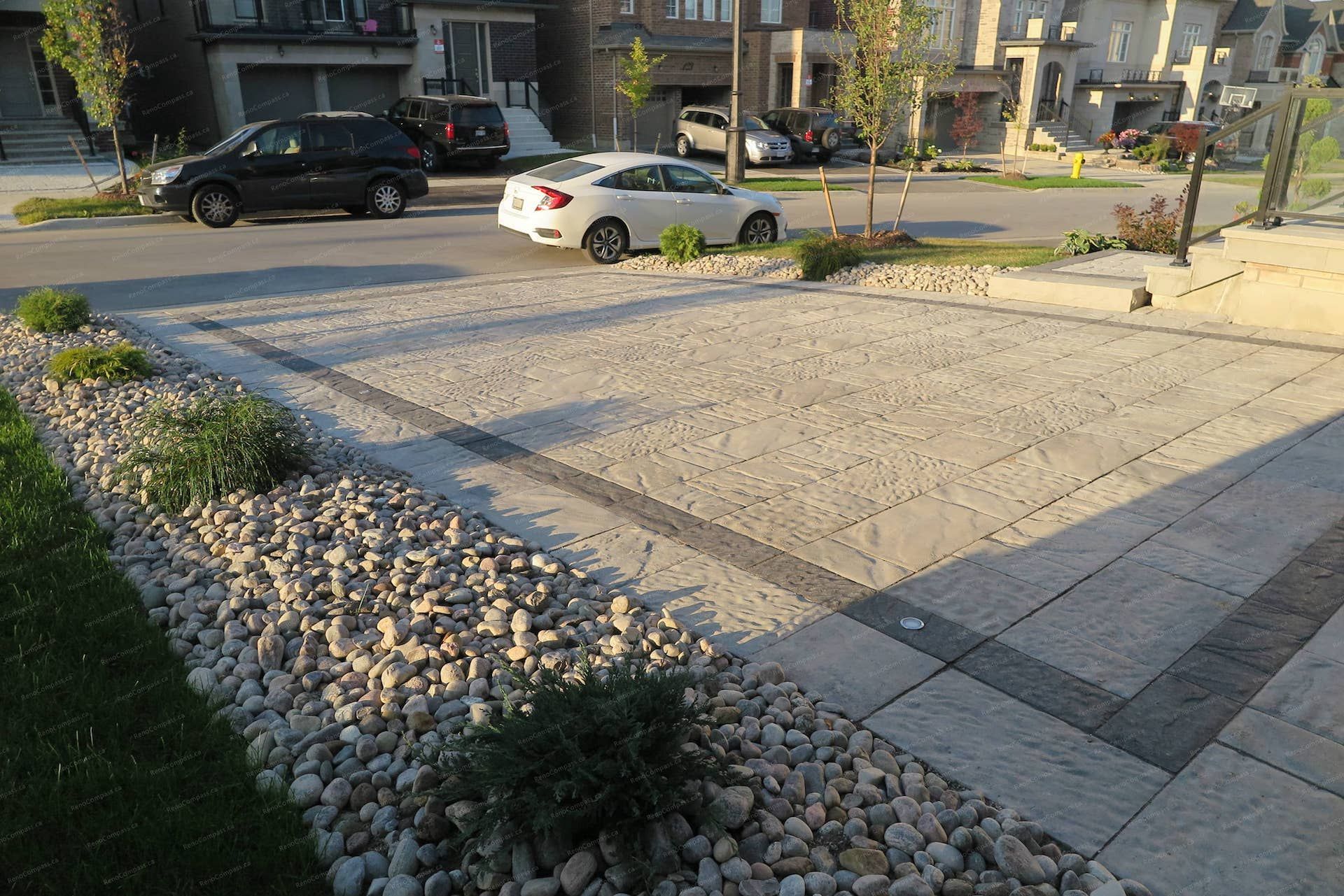 Front yard landscaping renovation for a detached home in Vaughan, featuring stamped concrete driveway paving, decorative stone borders, and modern landscape design with river rocks and low-maintenance plants. The project enhances curb appeal while creating a clean, durable driveway and elegant front yard entrance.