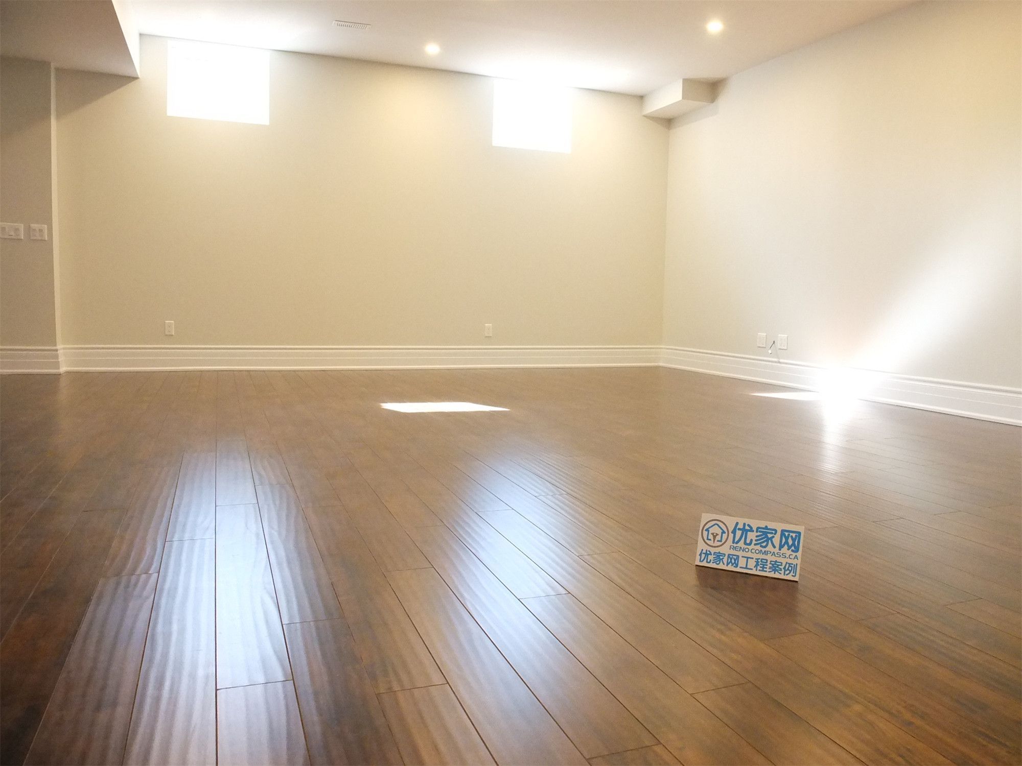 This Richmond Hill basement renovation features a spacious open-concept living area with dark hardwood flooring, recessed lighting, and bright basement windows. The natural light reflecting off the flooring enhances the sense of space, creating a warm and inviting environment ideal for family use or entertainment.