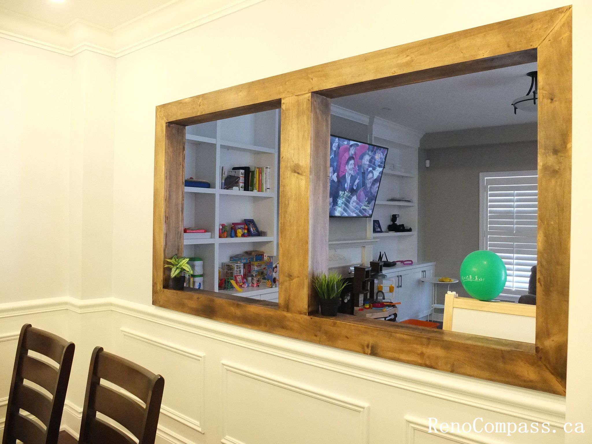 This Newmarket interior renovation highlights a bright and elegant dining room designed for both everyday meals and family gatherings. The space features classic wall wainscoting, dark hardwood flooring, and a modern rectangular pendant light fixture that adds a contemporary touch above the dining table. A large interior window opening with a warm wood frame connects the dining area to the adjacent living space, creating a more open and interactive layout. Completed by Reno Compass Inc., this project demonstrates thoughtful interior design and quality craftsmanship for modern family homes.
