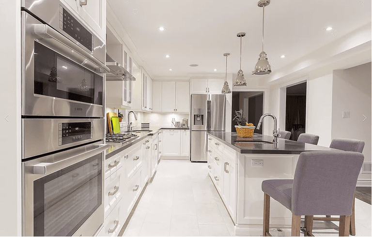 This bright, modern kitchen from our Vaughan full house renovation showcases white cabinetry, stainless steel appliances, and a spacious island with pendant lighting. Designed for both style and functionality, it reflects timeless elegance and open-concept living.