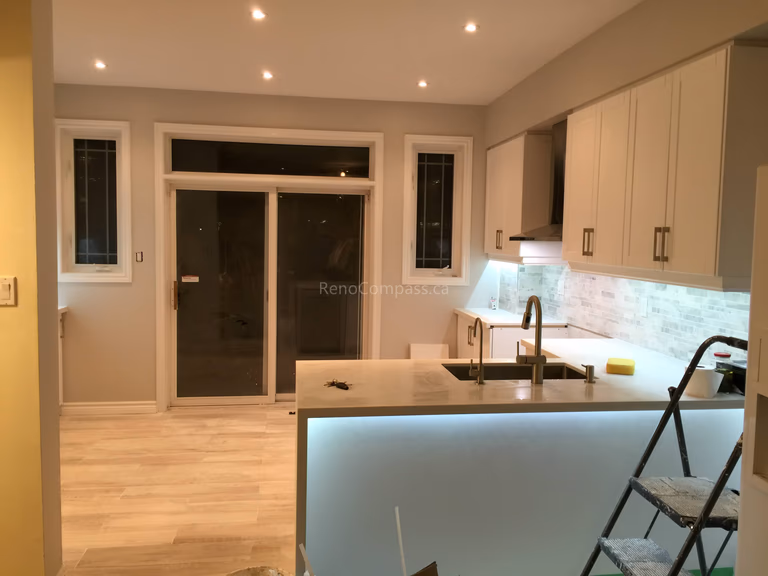 A modern open-concept kitchen interior renovation in Toronto featuring a large central island, integrated LED under-counter lighting, custom cabinetry, and light wood flooring. The design emphasizes functional flow, clean lines, and contemporary finishes, reflecting professional Toronto interior renovation and interior design expertise.