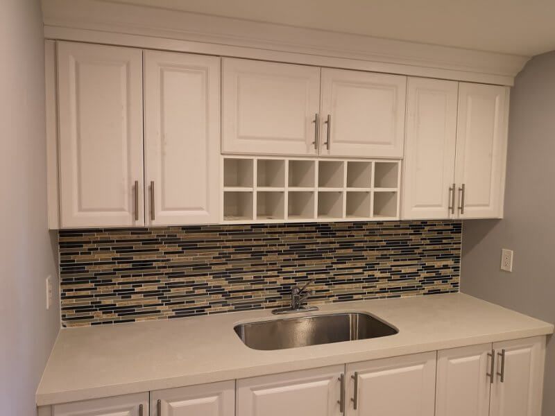 This Markham basement renovation features a modern kitchenette with white shaker cabinets, quartz countertop, mosaic tile backsplash, and built-in storage. Completed by a professional Toronto renovation company, the design enhances basement functionality and adds a stylish, practical space ideal for rental units, extended family living, or everyday convenience.