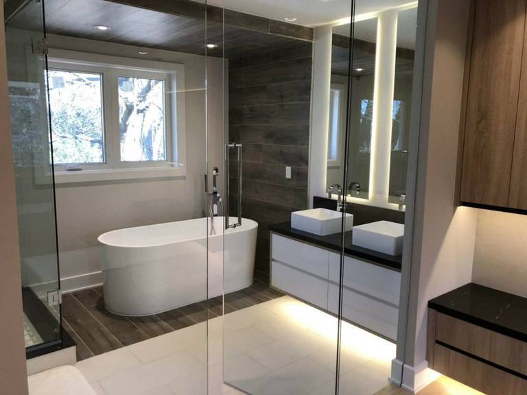 Upscale master bathroom renovation in Markham featuring a freestanding soaking tub, frameless glass shower, double vessel sinks, and custom floating vanity with under-cabinet LED lighting. The combination of wood accent walls, large-format tiles, and modern lighting creates a spa-inspired retreat that blends warmth, elegance, and everyday functionality for contemporary homes.