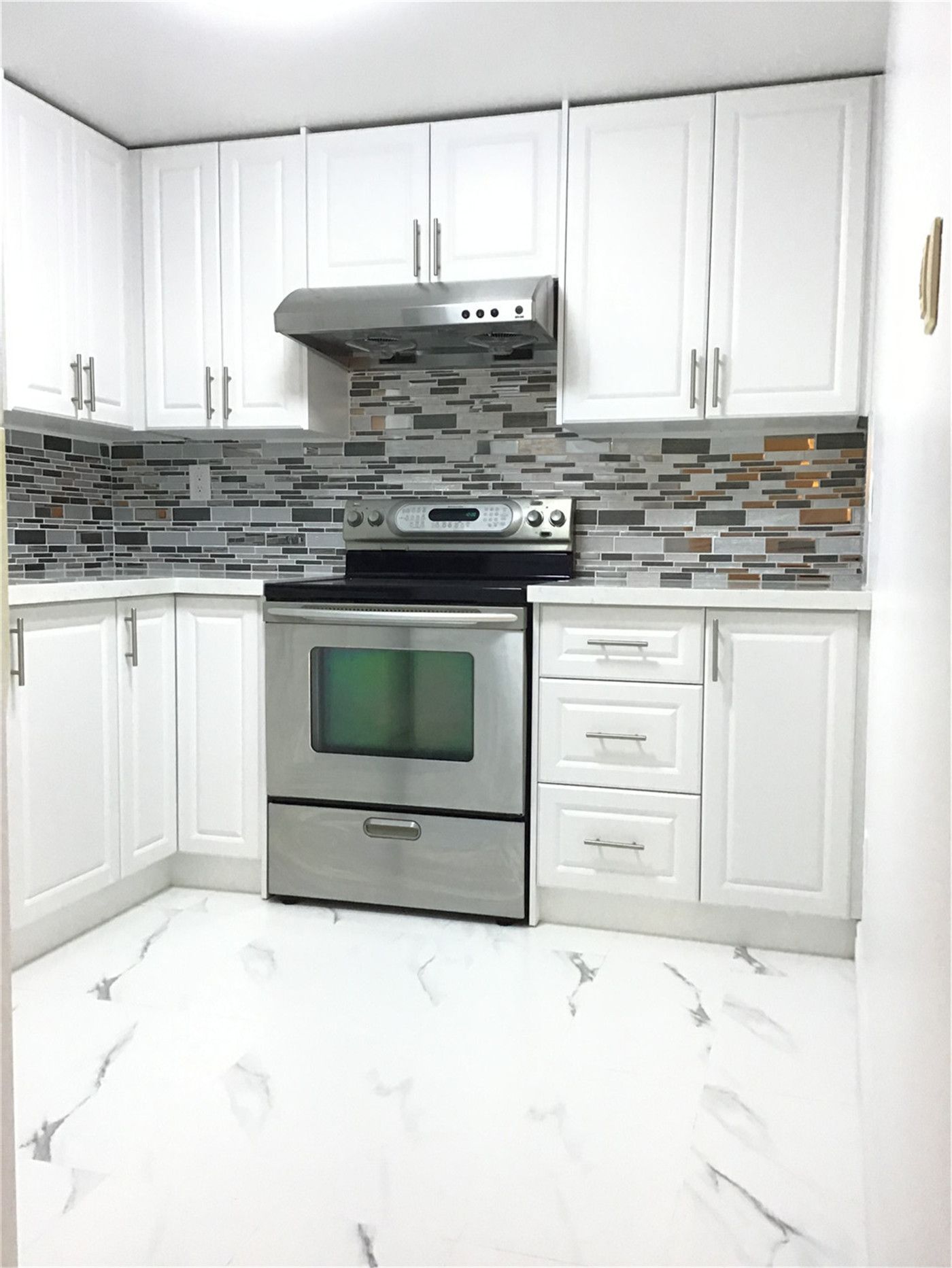 This Whitby basement renovation features a stylish L-shaped kitchen layout with crisp white shaker cabinets, stainless steel appliances, and a modern mosaic tile backsplash. The marble-look porcelain flooring enhances brightness and creates a clean, cohesive finish. Designed for functionality and efficiency, this basement kitchen is ideal for a secondary suite or rental-ready setup