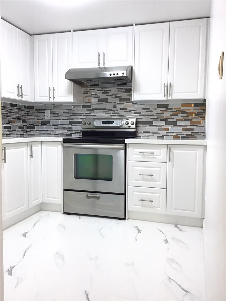 This Whitby basement renovation features a stylish L-shaped kitchen layout with crisp white shaker cabinets, stainless steel appliances, and a modern mosaic tile backsplash. The marble-look porcelain flooring enhances brightness and creates a clean, cohesive finish. Designed for functionality and efficiency, this basement kitchen is ideal for a secondary suite or rental-ready setup
