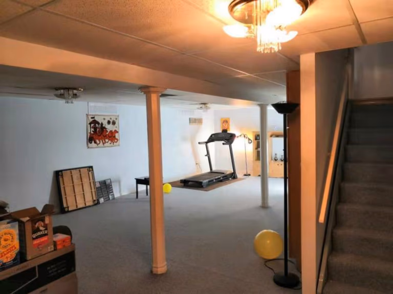 This Mississauga basement features a large open area with structural columns, carpet flooring, and a staircase access point. The space includes basic lighting and a home gym setup, highlighting its potential for a full renovation. A professional Toronto renovation company can transform this basement into a modern, multi-functional living space with improved layout, lighting, and finishes.