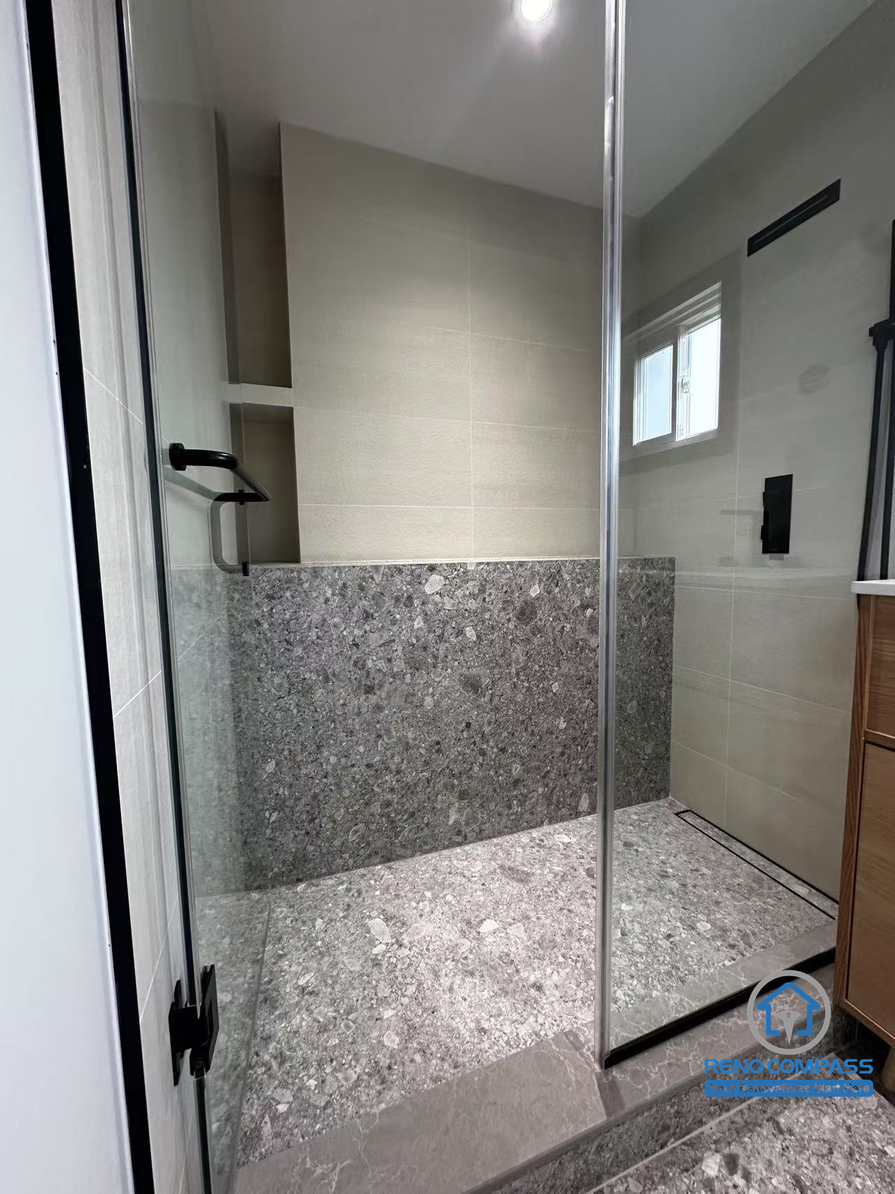 This image showcases the walk-in shower area in a Richmond Hill bathroom renovation. A frameless glass enclosure, textured stone flooring, and clean-lined wall tiles create a durable yet refined shower space. The minimalist black hardware adds contrast, while the thoughtful material selection enhances both functionality and visual depth. Designed and completed by Reno Compass, this shower reflects a modern bathroom renovation approach in the Greater Toronto Area.